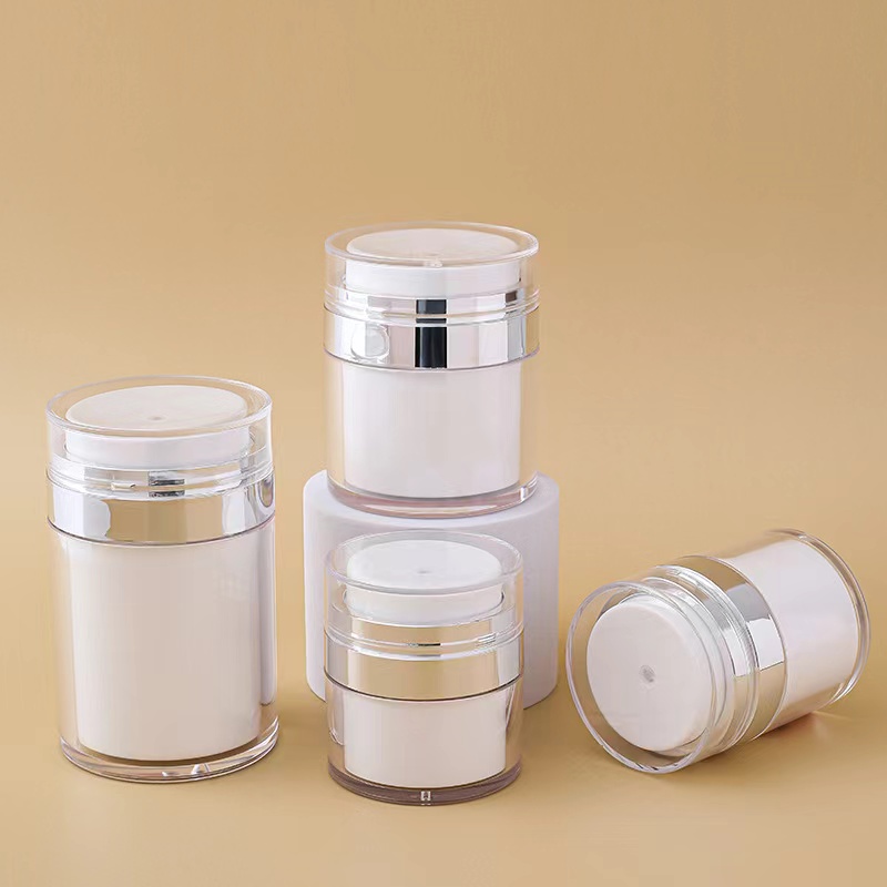 Four white cosmetic airless jars with transparent caps and metallic accents on a beige background.