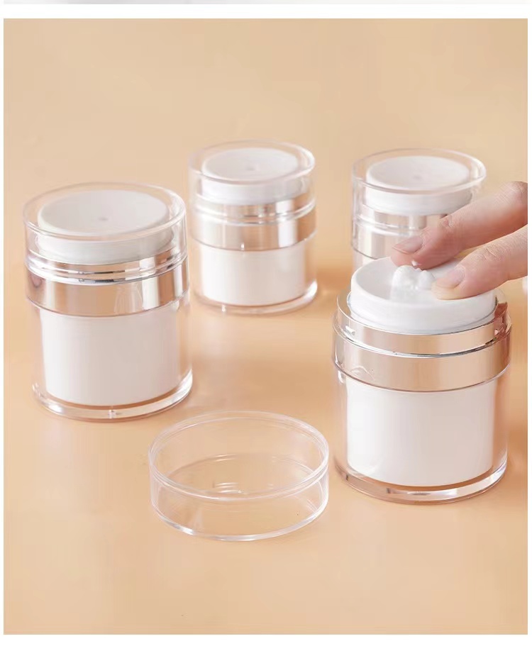 Four cosmetic airless jars, one being pressed to dispense cream, with transparent caps and metallic accents.