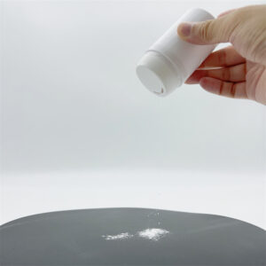 Hand dispensing white powder from plastic shaker container onto a surface.